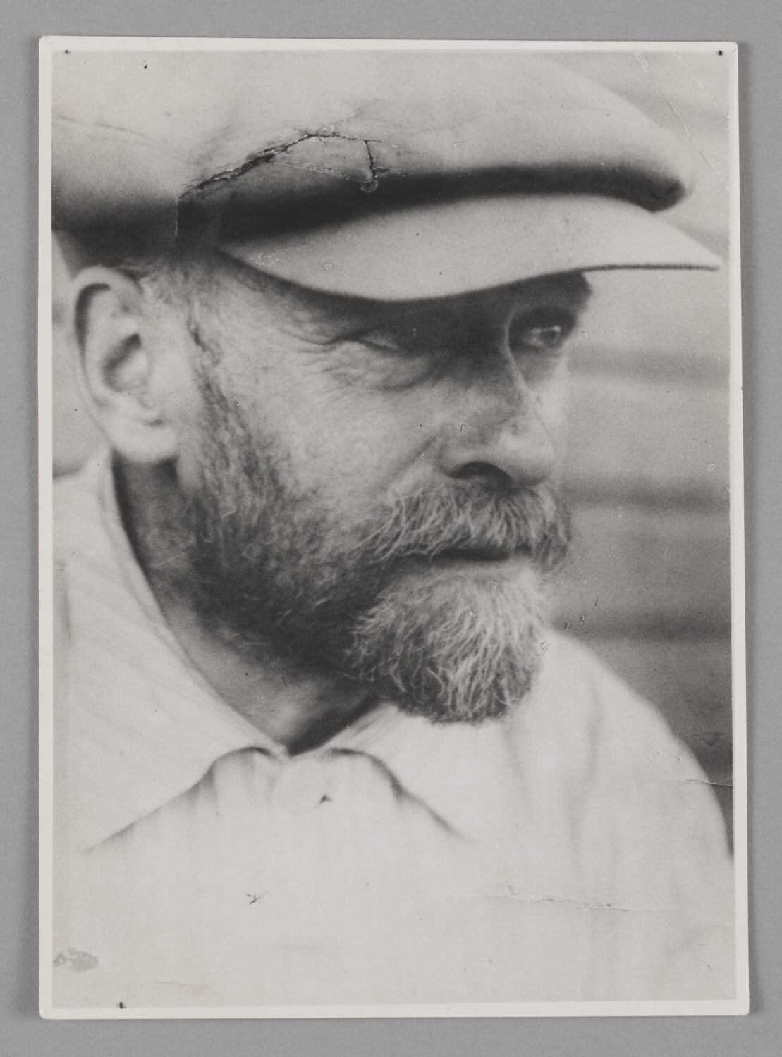 czarno białe zdjęcie, portret Janusza Korczaka, zarost: broda i wąsy, kaszkiet, biała koszula zapięta pod szyją